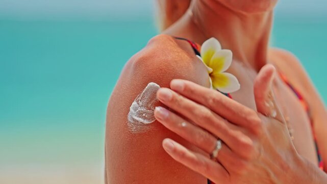 Young woman applying moisturizing sunscreen lotion on a shoulder with a beautiful ocean in the background. Skin care sun protection. Closeup