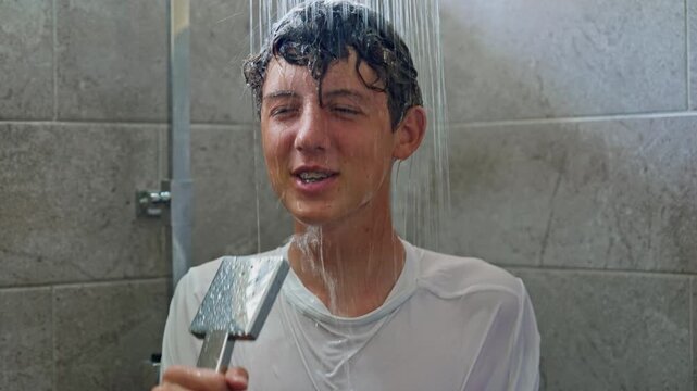 A cheerful teenage boy is having fun in the shower, singing his favorite song into the shower instead of a microphone