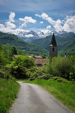 Country road to Erce mountain village in the middle of the greenery , with snow-capped peaks in the background. Ariege Pyrenees France