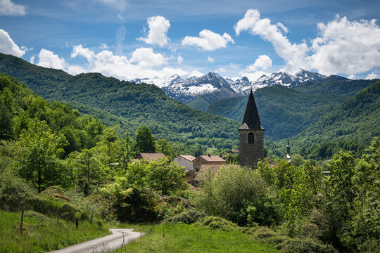 Bell tower of Erce mountain village in the middle of the greenery , with snow-capped peaks in the background. Ariege Pyrenees France
