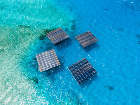 Aerial view of SolarSea floating solar power plant by Swimsol with four square solar panels on turquoise ocean water in Dharavandhoo, Baa Atoll, Maldives.