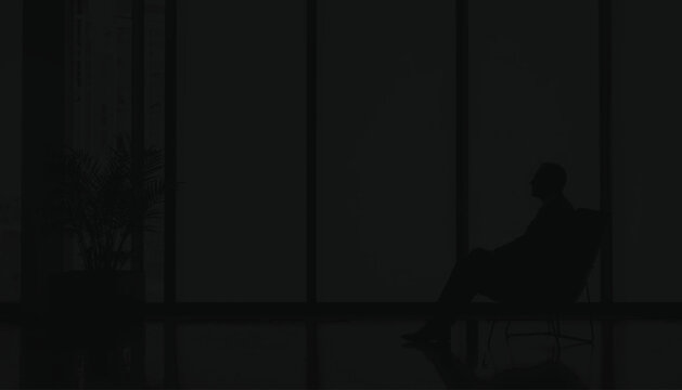 Executive sitting in a chair near a floor to ceiling window at night creates a somber silhouette that represents the heavy burden of responsibility and complex decision making in high level.
