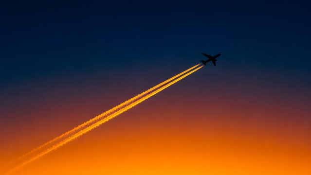 Silhouette airplane leaving contrails against vibrant sunset sky background.