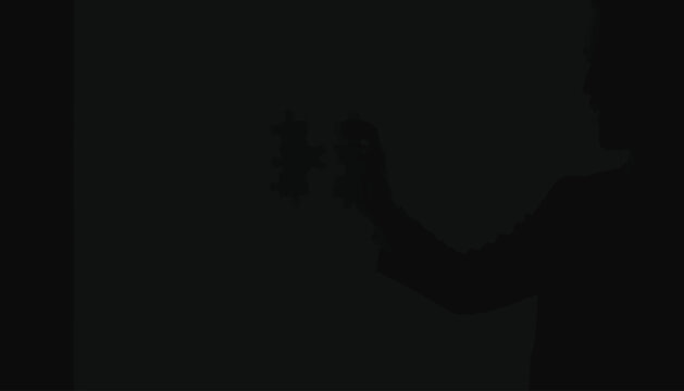 Businessman silhouette holds a small puzzle piece against a dark background to demonstrate strategic thinking, complex problem solving, mental challenge, logic, corporate planning, and teamwork.