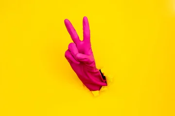 Magenta cleaning glove victory sign through torn yellow paper © GVS