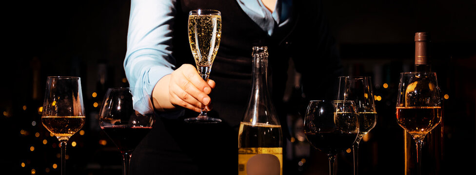 Professional sommelier holding glass of sparkling wine in bar. Selection and tasting of premium alcohol drinks.