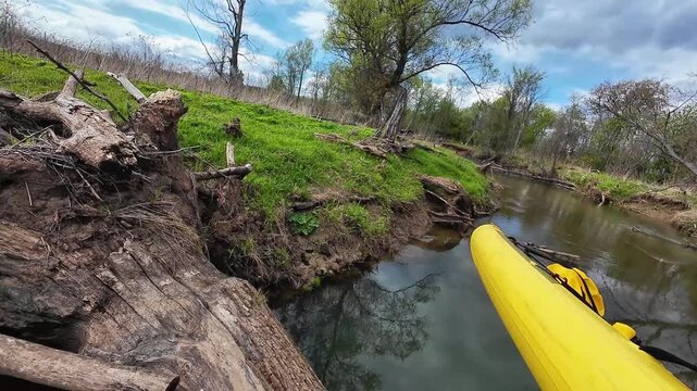 Closeup Of Kayak Navigating Roots. Kayak Near Log Barrier With Delicate Balancing Act Underway. An Adventurous Scene With Yellow Kayak Close To Tangled Log Obstacle On Green Bank