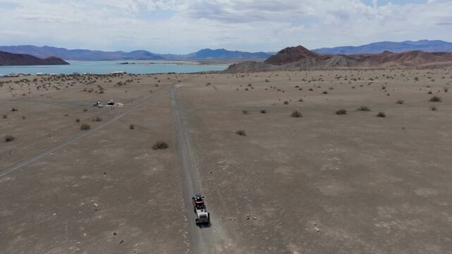 An SUV tows a teardrop camper from a Sea of Cortez campsite in Baja California, with the ocean in the background.