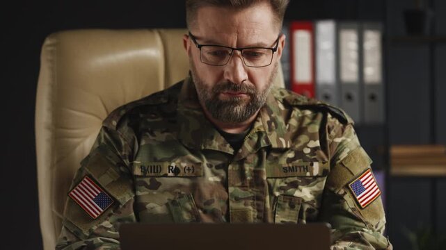 U.S. serviceman planning mission strategy while working on laptop in office