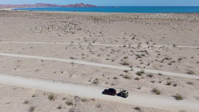 SUV pulls a teardrop camper trailer along dirt roads with ocean views during a camping trip in Baja California Mexico.