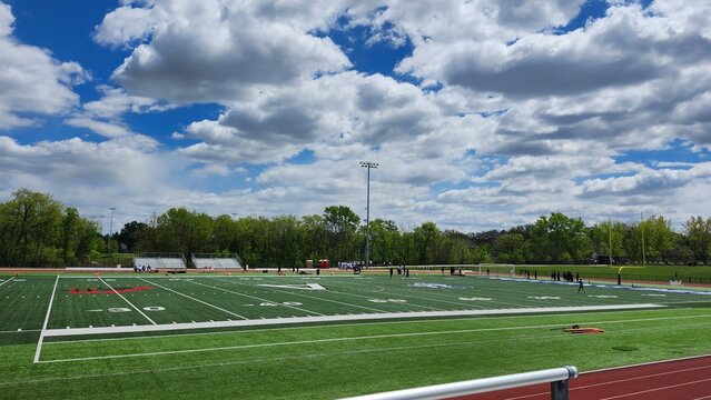 Empty outdoor football field and running track under cloudy blue sky