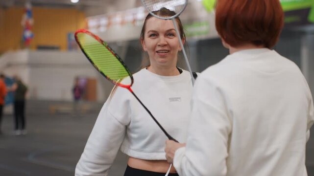 Relaxed athletes exchanging humorous remarks in casual sports attire during practice. Indoor tennis partners engaging in cheerful banter while preparing for match in comfortable clothing