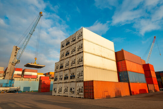 Large cranes stand ready to load containers from a terminal yard onto a cargo ship, showcasing a mix of standard and refrigerated units prepared for global maritime trade.