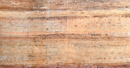 Rammed earth wall texture with horizontal layers of sedimentary rock and natural soil colors of orange brown and tan for architecture and sustainable building design background pattern material.