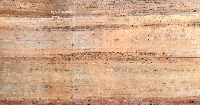 Rammed earth wall texture with horizontal layers of sedimentary rock and natural soil colors of orange brown and tan for architecture and sustainable building design background pattern material.
