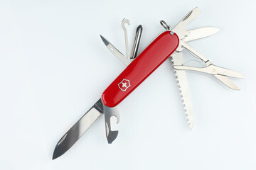 Classic red handled multitool pocket knife with various blades and tools displayed open on plain background © BrightLayer