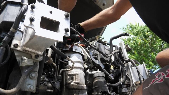 Male hands of repairer in gloves tightening bolts into car detail with electric tool outdoor. Arms of professional mechanic repairing auto at workplace. Repairman making maintenance of transport