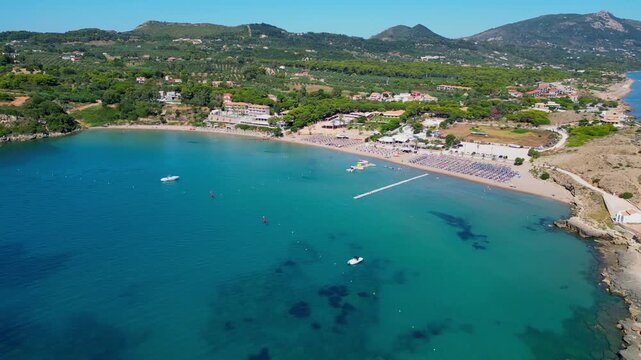 Spectacular view of St. Nicholas Beach in Vasilikos, Zakynthos. Crystal blue water, golden sand, and a small white hilltop chapel overlooking the Ionian Sea in a scenic Greek landscape.