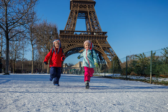 Two happy kids run in snow near the Eiffel Tower, Paris, France