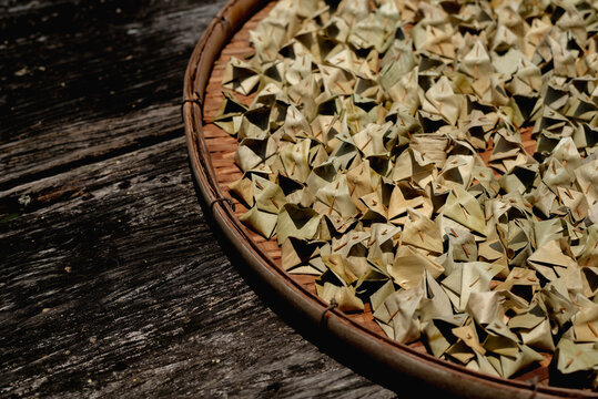 Traditional Thai desserts, Khanom Ja Mongkut or Sumpannee, are neatly arranged on a round wicker tray and placed on a rustic wooden surface to dry under natural sunlight.