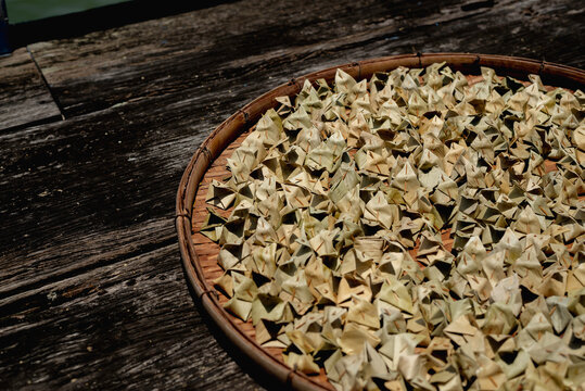 Traditional Thai desserts, Khanom Ja Mongkut or Sumpannee, are neatly arranged on a round wicker tray and placed on a rustic wooden surface to dry under natural sunlight.