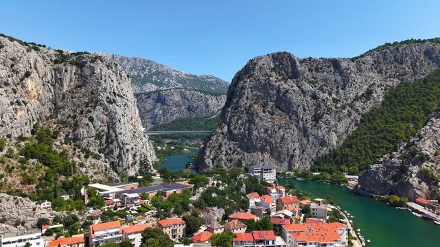 Aerial view of the Cetina River canyon and Omis town in Croatia, scenic mountain landscape with bridge and river flowing through limestone cliffs under clear blue sky