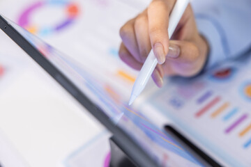 Fototapeta premium Focused professional hand utilizing white digital stylus pen on modern tablet computer screen for detailed finance analysis with colorful business chart graphic background in office