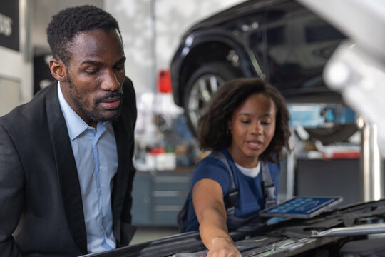 Woman mechanic explaining car problem to client, showing digital diagnostics on tablet. Inclusivity and professionalism in the auto industry.