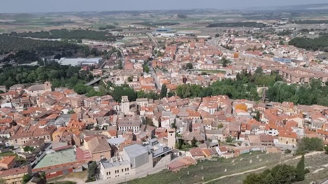 Aerial view of Pe&ntilde;afiel, Spain, featuring its dense urban landscape with terracotta roofs, historic church towers, and modern architecture integrated into the traditional Castilian town center.