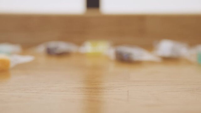 Picking up wrapper amid colorful sweets. Person gently removes wrapper from counter with vibrant candies behind. Meticulous individual carefully tidies up with candies softly blurring in background