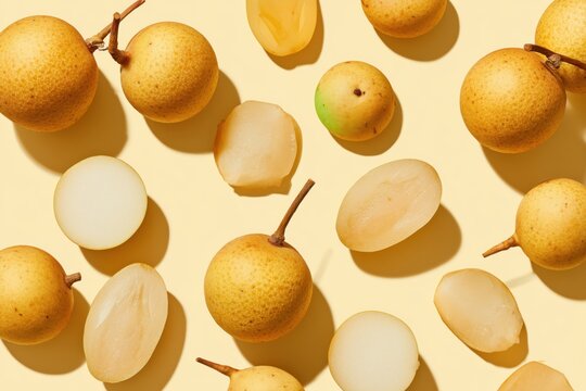 Top-down arrangement of whole and halved asian pears on pale yellow background with soft shadows