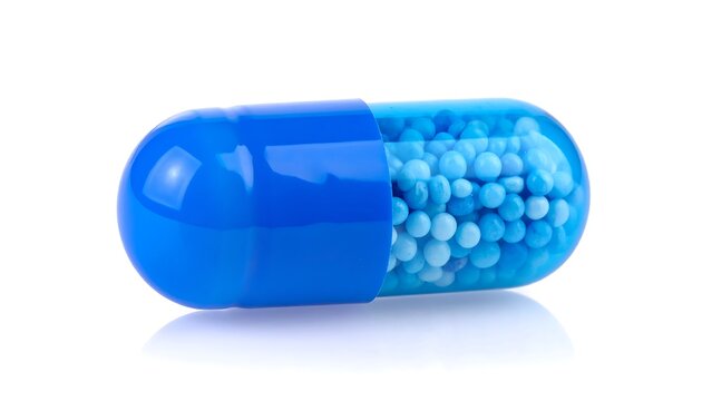 Macro shot of a single blue capsule containing small, round, light blue granules, sitting on a white background with a subtle reflection