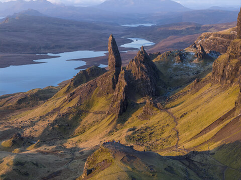 Aerial view of The Storr rock formation with people standing on a ridge and a lake in the background during golden hour in Isle of Skye, Scotland, United Kingdom.