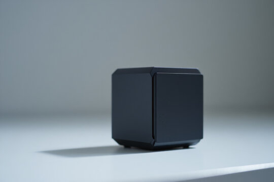 Black cube shaped electronic device on a white surface with soft lighting