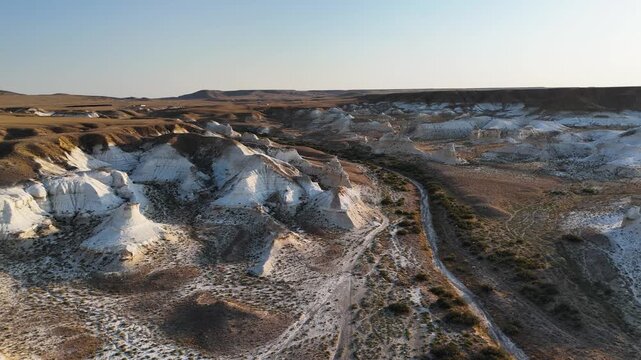 Drone view of a hilly desert valley featuring white and brown chalk outcrops. Footage captures the ancient Tethys Ocean floor in the Mangystau region, Kazakhstan. Unique rock formations and contrastin