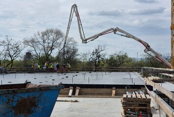 Construction workers pouring concrete on a building floor slab with a concrete pump boom overhead. © Mevhis
