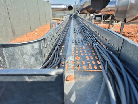 Low angle close-up of organized and bundled electrical cables in a metal cable tray on a rooftop mechanical plant.