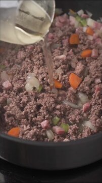 Pouring white wine into pan with meat and vegetables for ragu