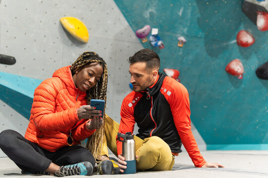 Diverse couple discussing route on smartphone at bouldering gym