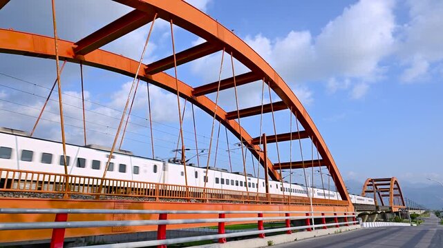 A white train travels across a vibrant red arched bridge in Yuli, Hualien, Taiwan, set against a clear blue sky with mountains in the background.