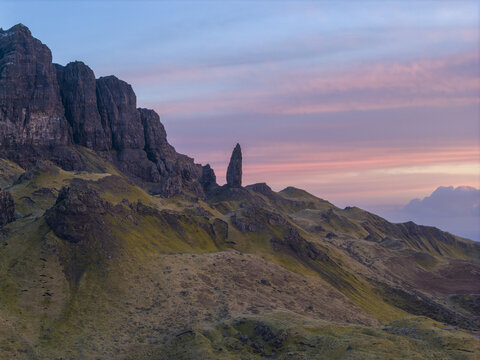 Aerial view of The Storr rock formation with its iconic pinnacle and grassy slopes under a vibrant sunset sky in Isle of Skye, Scotland, United Kingdom.