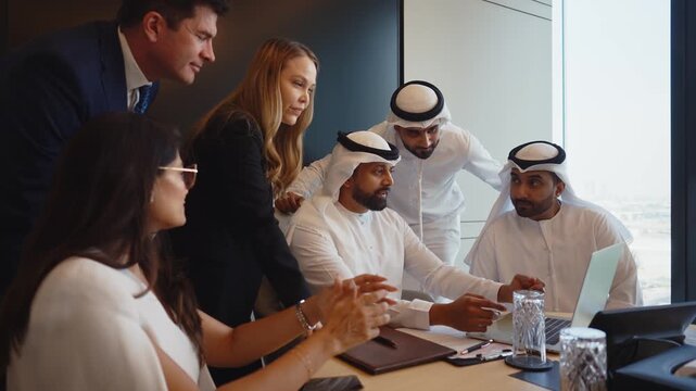 Corporate business event with emirati and western business people international business team collaborating around a conference table reviewing strategy documents and laptops