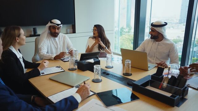 Corporate business event with emirati and western business people international business team collaborating around a conference table reviewing strategy documents and laptops