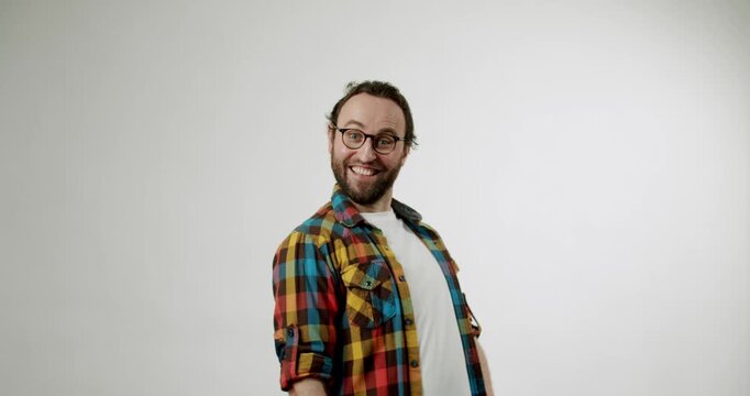 Surprised man pointing at the camera. He has a beard and is wearing a colorful plaid shirt over a white t-shirt. He looks excited and happy, against a white background in a studio setting.