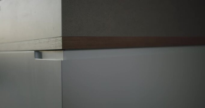 Close-up of minimalist white kitchen cabinets with a concrete countertop and light wooden trim. The smooth surfaces and simple design create a modern and sleek aesthetic. contemporary kitchen design.