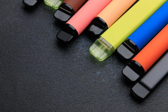 Various electronic cigarettes arranged in different colors on a dark surface for display and examination