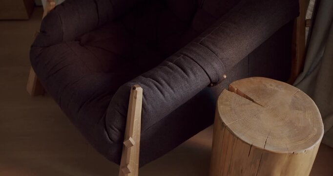 Cozy living room interior detail with comfortable armchair and unique side table made from a tree trunk. Warm, inviting atmosphere with natural materials and textures.