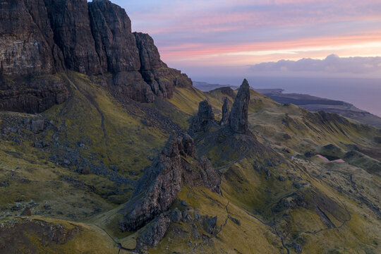 Aerial view of The Storr rock formations and green grassy slopes under a pink sunset sky in Isle of Skye, Scotland, United Kingdom.
