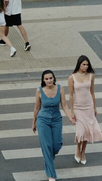 Two fashionable women cross the street on a crosswalk. Stylish friends on a stroll through the city. Summer vibes and urban lifestyle. Slow-motion shot adds a touch of elegance.