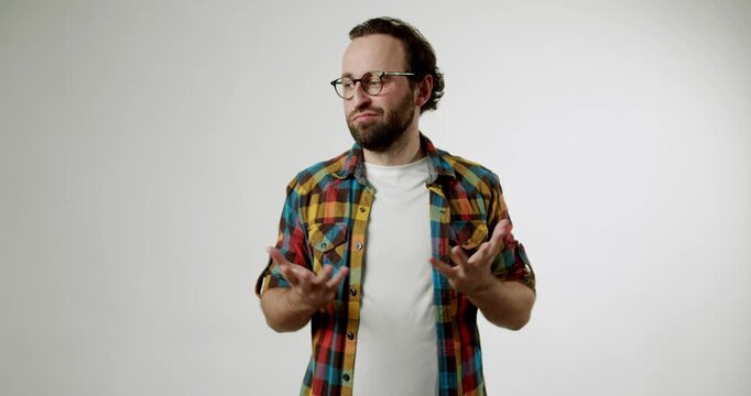 Man in colorful shirt, glasses, and beard holds his stomach with both hands, standing against a white backdrop. He winces, looks from side to side, and shows discomfort, possibly from stomach pain